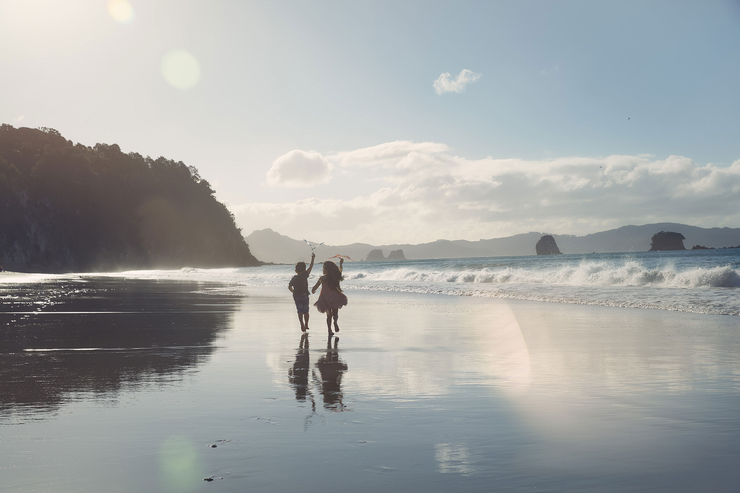 boy and girl running down beach with kite nz