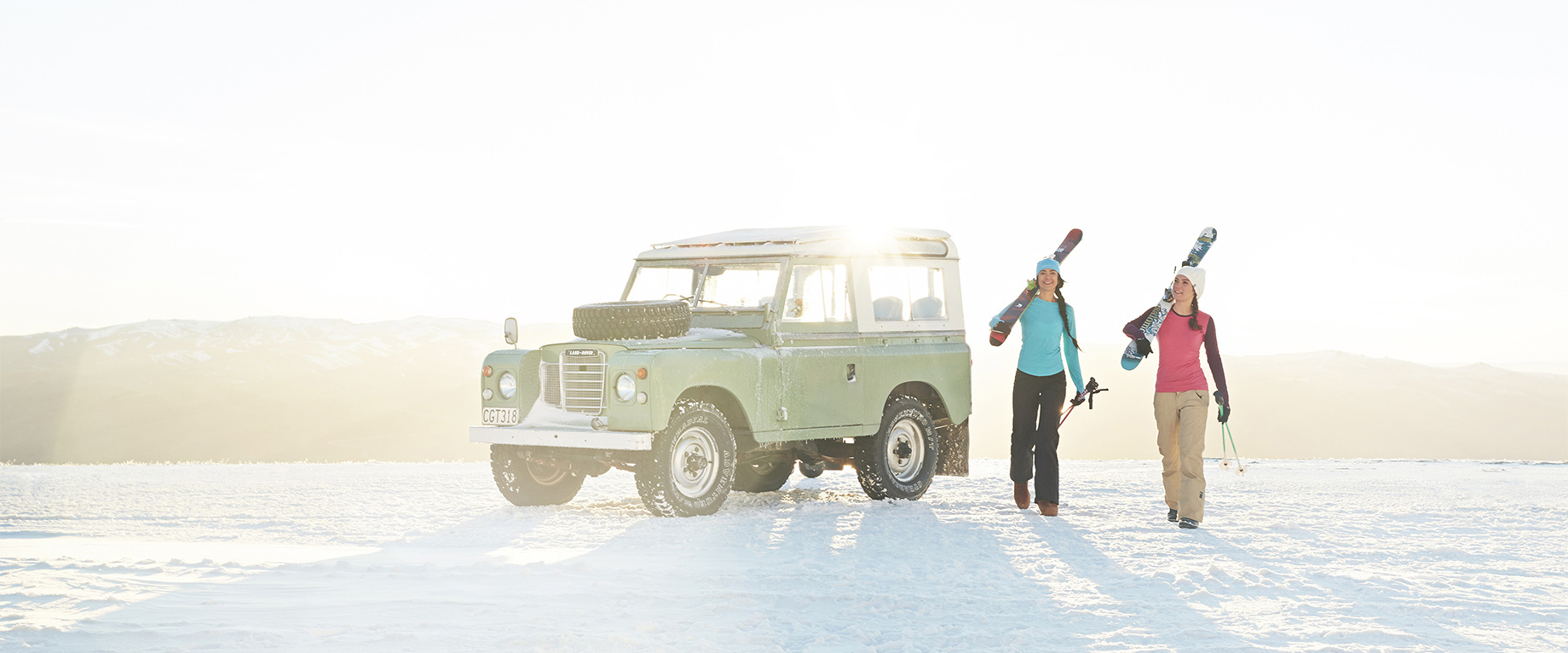 two woman in snow with snowboards jeep