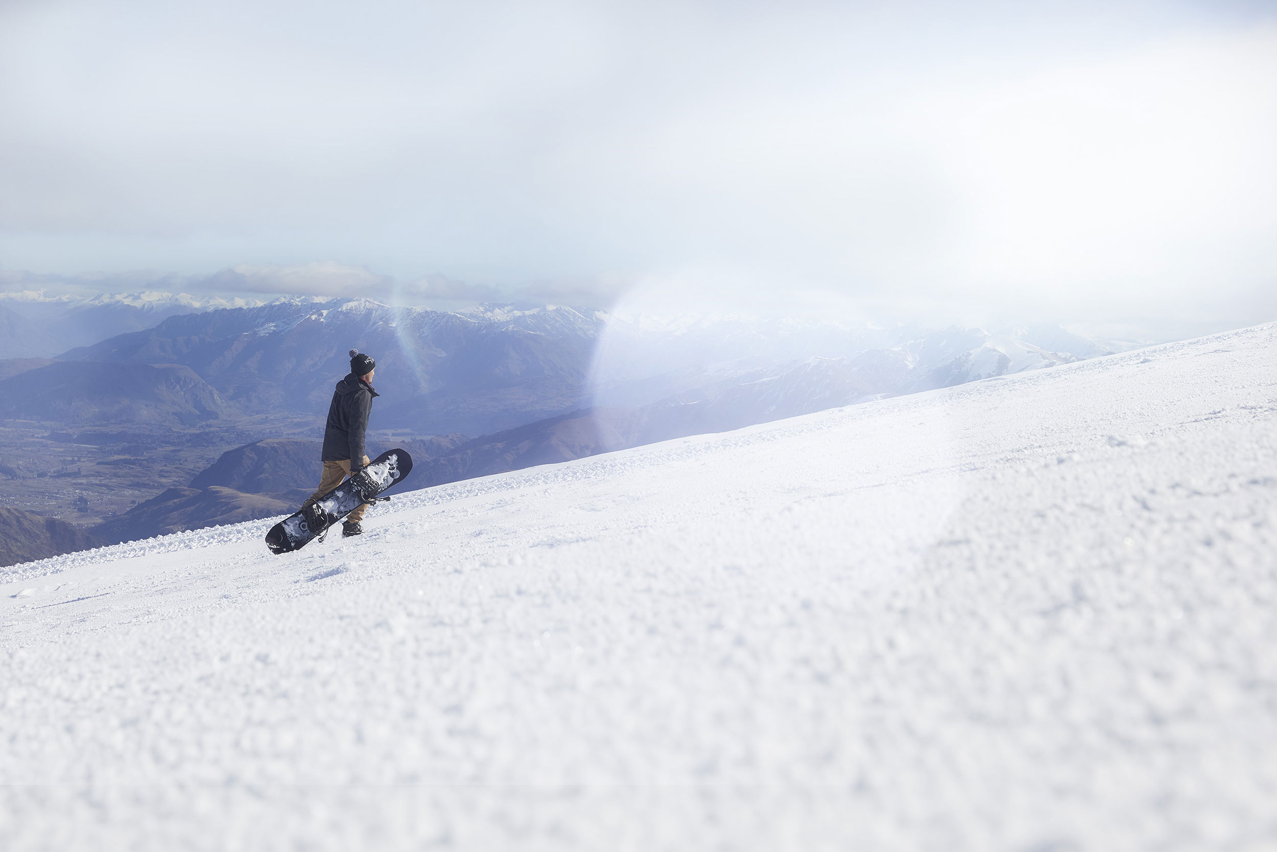 man with snowboard walking up mountain with snowboard nz