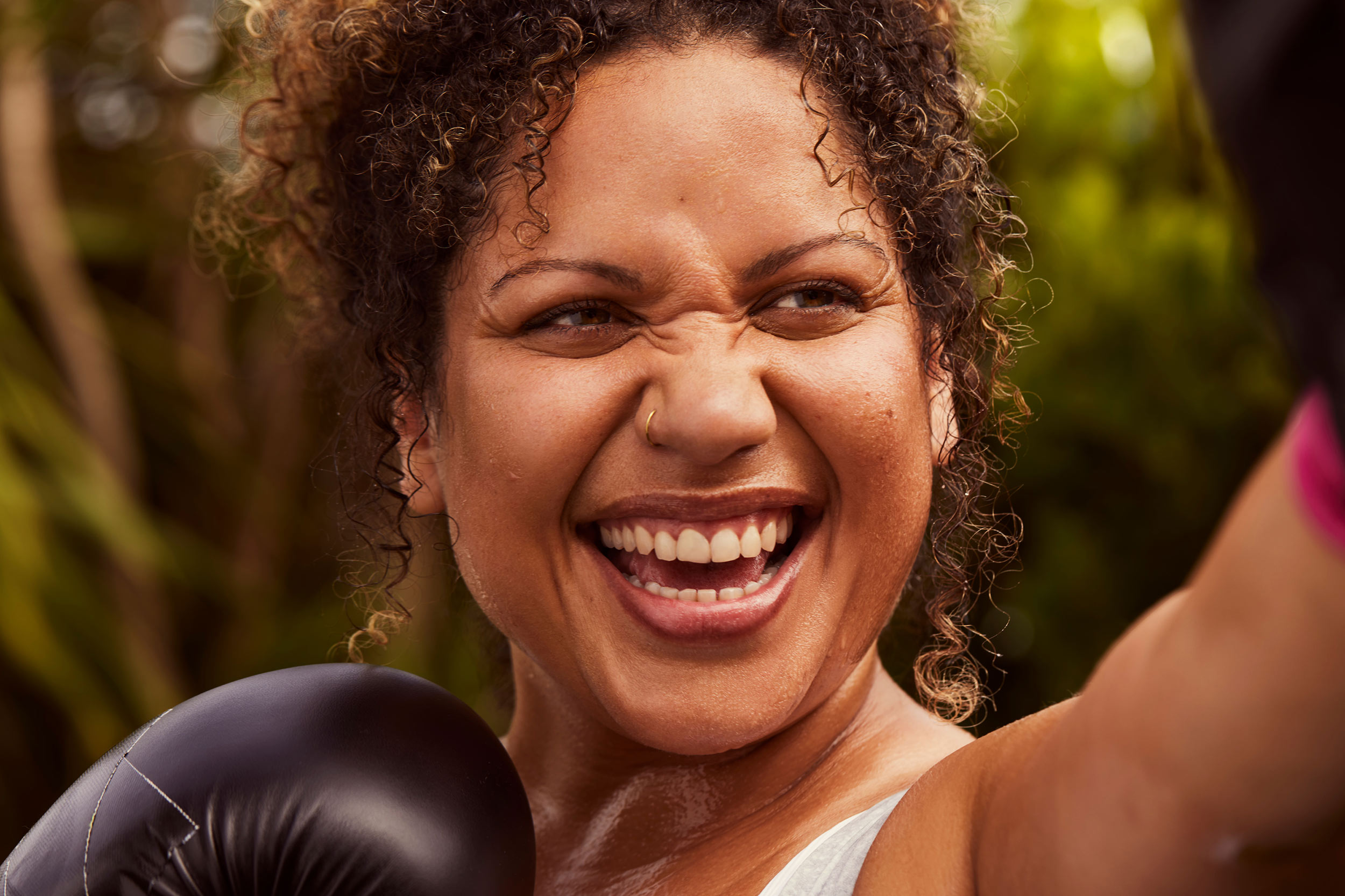 Curly haired woman boxing outside and smiling Essano