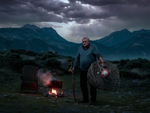 Old man holding Crayfish pot in front of an open air fire